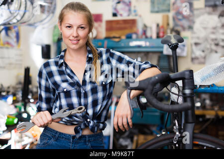 Portrait of happy girl who is fixing her bicycle indoors Stock Photo