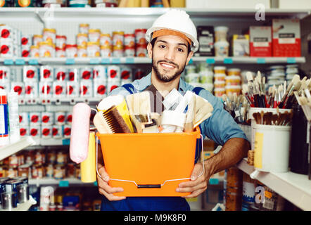 Cheerful  workman holding basket with picked tools in paint store Stock Photo