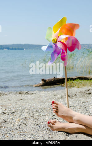 Children's windmill and female legs at the beach in summer. Stock Photo