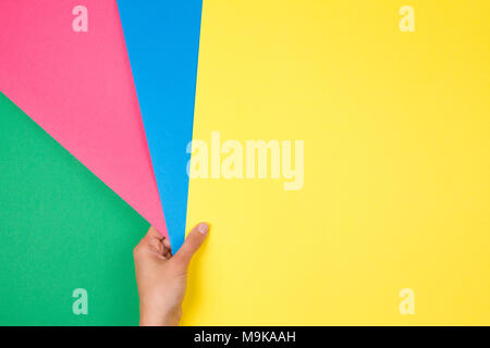 Color papers geometry flat composition with female hand holding green, pink, blue and green paper samples. Stock Photo