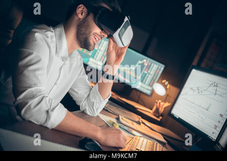 Young bearded man trader at office sitting at table wearing virtual reality headset smiling cheerful Stock Photo