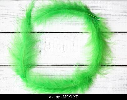 Minimalist Easter concept with soft frame made of neon green feathers. White painted wooden background and copy space. Top view and flat layout Stock Photo