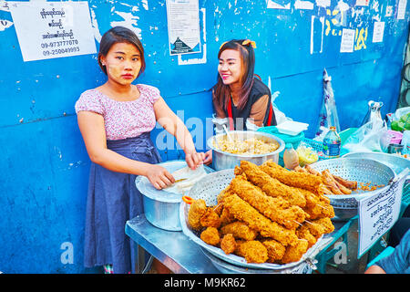 YANGON, MYANMAR - FEBRUARY 14, 2018: The young food vendors in Chinatown market stall offer deep fried cicken on skewers, rice with vegetables and oth Stock Photo