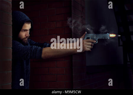 Hooded criminal in a dark brick alley fires a handgun with speeding bullet leaving the chamber with smoke and muzzle flash Stock Photo