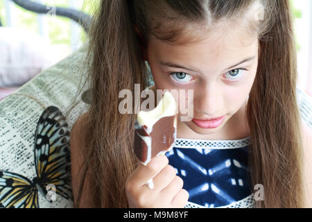 Young girl / child eating a messy dripping chocolate ice cream on a stick. Extreme shallow depth of field with selective focus on girls eyes and not i Stock Photo
