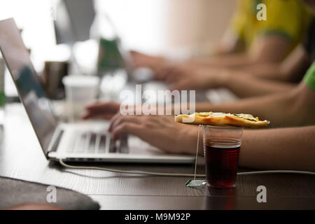 A plastic glass of tea and a piece of pizza on the table at the programmers. Lunch programmer. Stock Photo