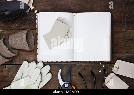 Gardening journal surrounded with tools, tomato seeds and flower pots on a rustic wooden table. Image shot from above in flat lay style. Stock Photo
