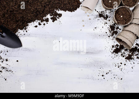 Gardening tools, seedling peat pots, seeds and soil on a white wooden table. Image shot from above in flat lay style. Stock Photo