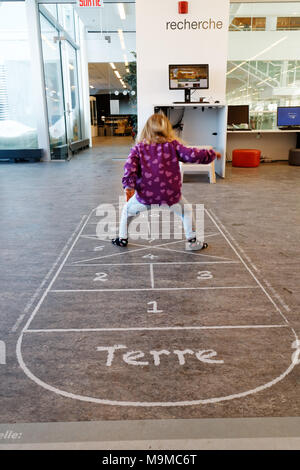 A little girl (3 yrs old) playing hopscotch on an indoor hopscotch game in a public library in Quebec Canada Stock Photo