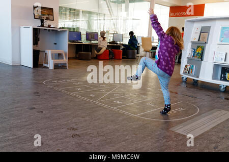 A little girl (3 yrs old) playing hopscotch on an indoor hopscotch game in a public ibrary in Quebec Canada Stock Photo