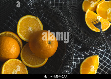 Top view of cut oranges in black wire bowl on black table. Stock Photo