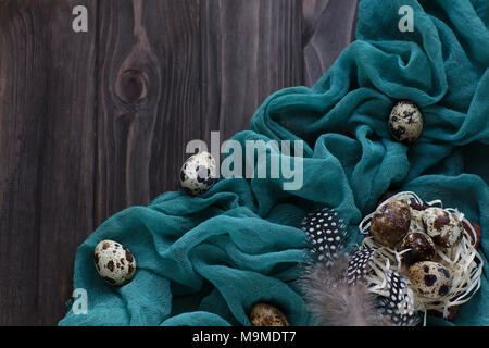 Easter decoration feathers quail eggs, green fabric on wooden brown background Stock Photo