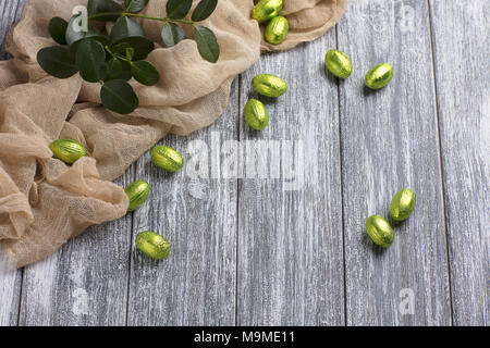 Easter chocolate eggs in foil with beige fabric on gray wooden background Stock Photo