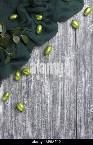 Easter chocolate eggs in foil with green fabric on gray wooden background Stock Photo