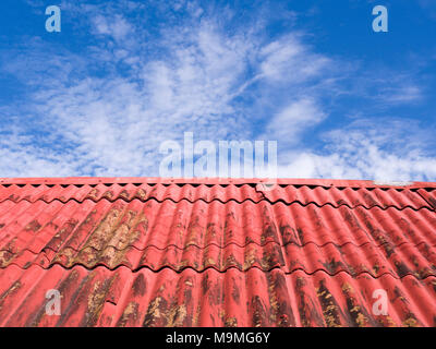 Textures, red and rusting roof and the sky: A corrugated red roof starting to rust against a mackerel sky. Stock Photo