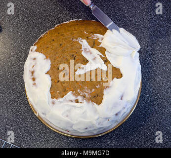 Icing and decorating a Carrot Cake: Spreading the white icing with a knife early stages. Stock Photo