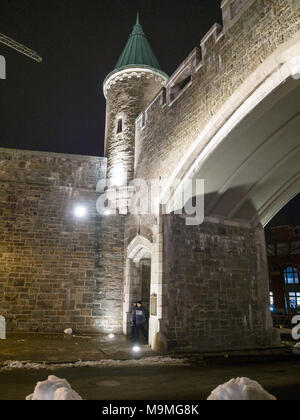 St John's Gate, an entrance to Old Quebec: The ancient stone gate in this walled city from the outside.  A couple dressed warmly walks out of the city. Stock Photo