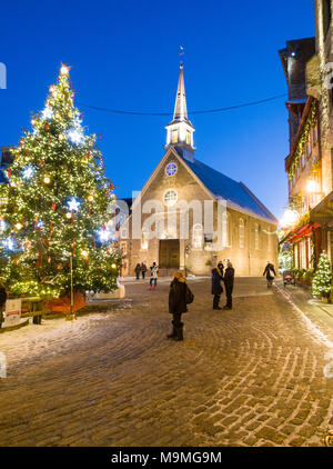 Notre Dame des Victorires and Christmas Tree: The small church in the touristic section of Lower Quebec with a large lit christmas tree in the square. Tourists watch and wander. Stock Photo