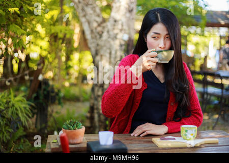 young woman sitting on a table and drinking a cup of coffe in the garden Stock Photo