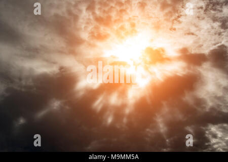 Dramatic background with warm sun rays penetrating dark clouds. Stock Photo