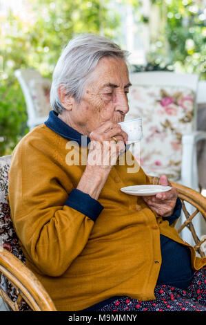 Elderly woman sitting and drinking Turkish coffee in the balcony on a sunny day. Stock Photo
