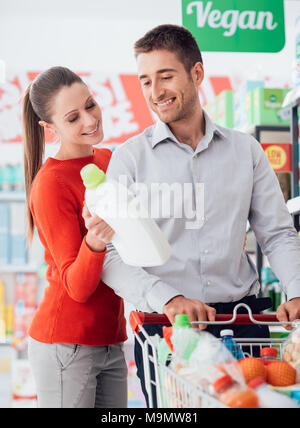 Young couple doing grocery shopping at the supermarket, they are reading a label on a detergent bottle Stock Photo