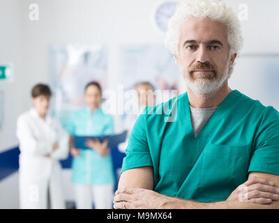 Professional medical team working at the hospital and surgeon posing in the foreground with arms crossed Stock Photo