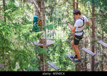 Teenager having fun on high ropes course, adventure, park, climbing trees in a forest in summer