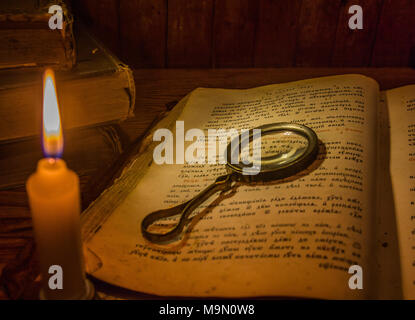 An open ancient prayer book and a magnifying glass on its open pages under the light of a candle Stock Photo