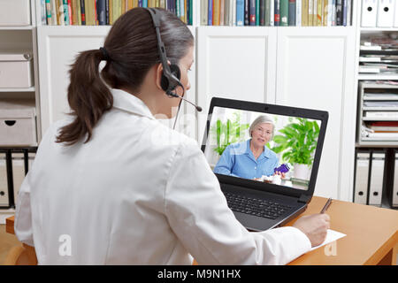 Doctor of geriatrics in her surgery office with headset in front of her laptop during a video call with a senior patient about her prescribed drugs. Stock Photo