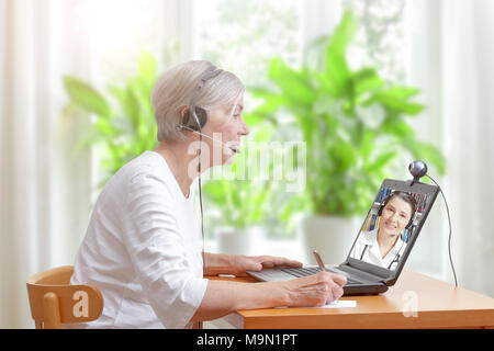 Senior woman in her living room in front of a laptop making notes during a video call with her female doctor Stock Photo