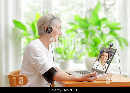 Senior woman in her living room in front of a laptop checking her blood pressure during a video call with her doctor of cardiology Stock Photo