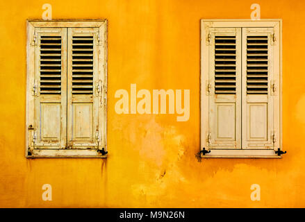Yellow wall with two windows with shutters in Plaka district in Athens, Greece Stock Photo