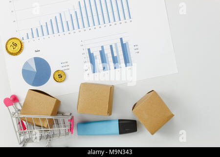 Table top view aerial image of business finance background.Flat lay graph growth up with coin money & shopping cart or trolley on modern white wood.Sa Stock Photo