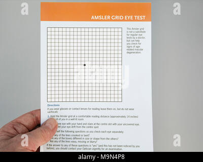 Senior elderly person hand holding and looking at an Amsler Grid Eye Test card to check eyesight for Age-Related Macular Degeneration in eyes. UK Stock Photo