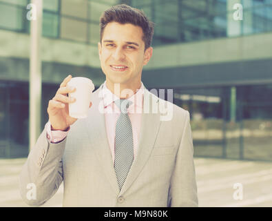 Portrait of young successful businessman drinking coffee near large factory Stock Photo