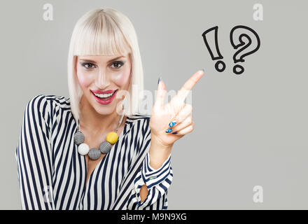 Happy smiling woman looking at written drawings of question marks on gray background. Idea Concept Stock Photo