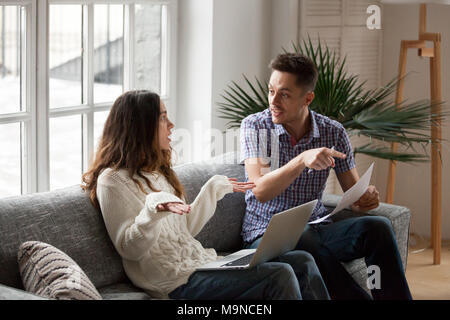Young couple arguing about high domestic bills to pay with laptop and documents, unhappy family having conflict disagreement discussing unpaid debt or Stock Photo
