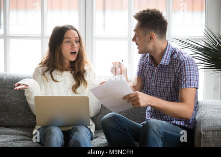 Worried unhappy couple arguing about debt or high domestic bills with laptop and documents, young family having quarrel discussing wasting money bankr Stock Photo