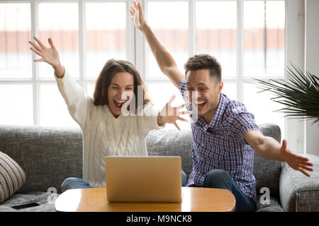 Young couple feeling excited by online win looking at laptop screen, happy man and woman celebrating victory watching video, screaming enjoying good n Stock Photo