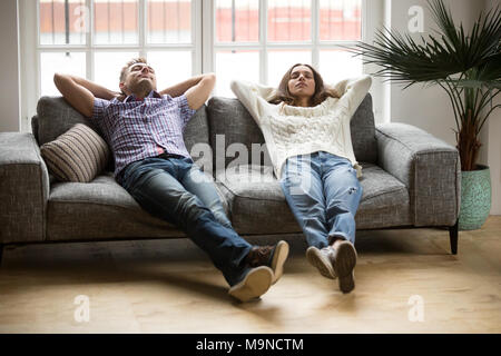 Young couple relaxing having nap or breathing fresh air, relaxed man and woman enjoying rest on comfortable sofa in living room, happy family leaning  Stock Photo