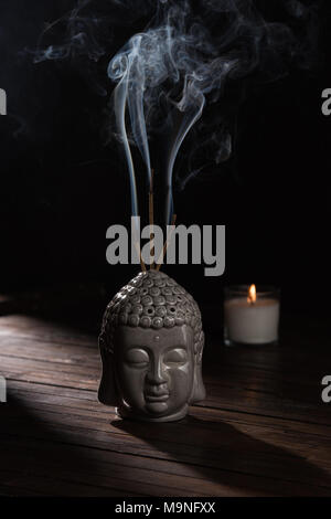 sculpture of buddha head with burning incense sticks and candle on table Stock Photo