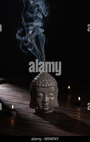 sculpture of buddha head with burning incense sticks and candles on table Stock Photo