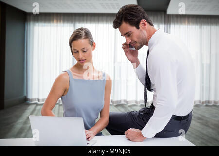 Composite image of businessman talking on phone while discussing with colleague over laptop against Stock Photo