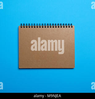 notebook on a black iron spring with brown empty sheets on a blue background, close up Stock Photo