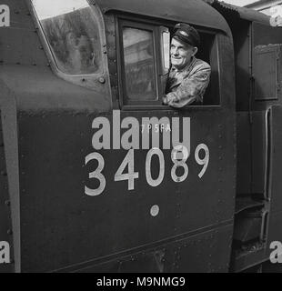 Early 1950s, historical picture of a train driver with cap in the engine cabin of a Southern Railways steam locomotive, 602 Squadron (34089) England, UK. Built in 1948, and named in honour of the RAF squadron of the 'Battle of Britain', this 4-6-2 light pacific locomotive was in service until 1967. Over 1,000 new steam locomotives were built at this time, as the British government of the day (Labour) wanted to use domestically produced coal, thereby keeping the coal miners in employment post-war. Stock Photo