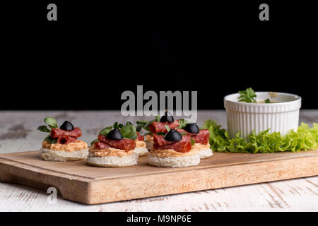 Delicious canapes with salami, olives and spices on a woody background Stock Photo