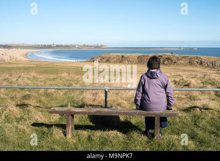 Woman sitting looking across the Tyne estuary from South Shields towards Tynemouth, north east England, UK