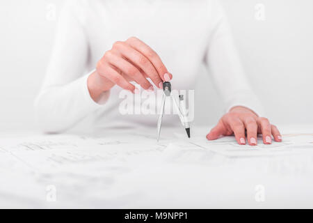 The woman holds in hands compass, over table with drawings. Stock Photo