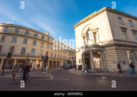 Sunny street scene in Bath at the junction of New Bond Street and Walcot Street with shoppers and cars waiting at traffic lights Stock Photo